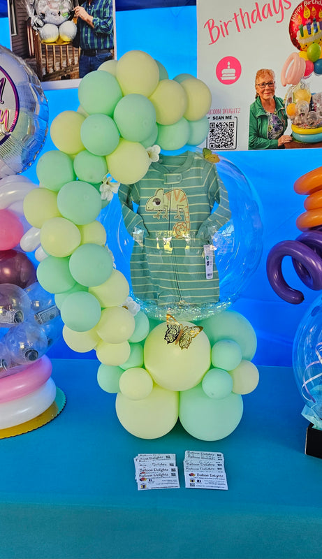 This baby shower Hug Balloon features over 50 balloons, a cute onesie provided by the customer, along with delicate butterflies and silk flowers.